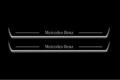 Two long door sill plates with Mercedes-Benz lettering and edges illuminated in white, straight-on view on a dark background.