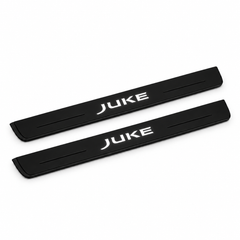 Catalogue illustration of two black Matte PRO front door sill plates with illuminated JUKE lettering on the top surface. Edges are unlit; rear plates for FRONT+REAR are not pictured. Final dimensions are selected for Nissan Juke F15 during manufacture.
