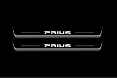 Two long door sill plates with Prius lettering and edges illuminated in white, straight-on view on a dark background.
