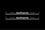 Two long door sill plates with Quattroporte lettering and edges illuminated in white, straight-on view on a dark background.