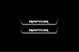 Two short door sill plates with Raptor lettering and edges illuminated in white, straight-on view on a dark background.