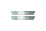 Two short silver-finished door sill plates with Raptor lettering on a light background, straight-on view.