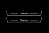 Two long door sill plates with R Design lettering and edges illuminated in white, straight-on view on a dark background.
