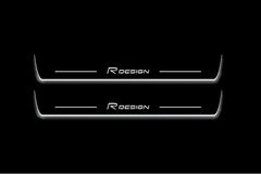 Two long door sill plates with R Design lettering and edges illuminated in white, straight-on view on a dark background.