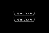 Two short door sill plates with Rivian with diamond emblems lettering and edges illuminated in white, straight-on view on a dark background.