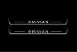 Two long door sill plates with Rivian with diamond emblems lettering and edges illuminated in white, straight-on view on a dark background.