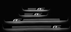 Four dark door sill plates with offset R-Line emblems and white illuminated horizontal lines and edges, straight-on view.