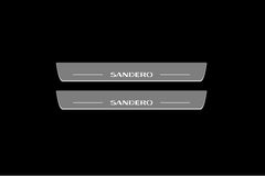 Catalog illustration of two gray door sill plates with Sandero lettering against a black background.