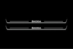 Two long door sill plates with Škoda lettering and edges illuminated in white, straight-on view on a dark background.