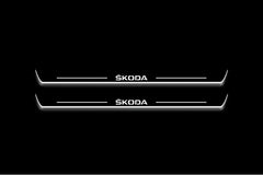 Two long door sill plates with Škoda lettering and edges illuminated in white, straight-on view on a dark background.