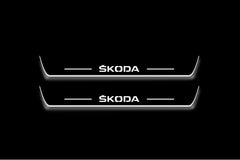 Two long door sill plates with Škoda lettering and edges illuminated in white, straight-on view on a dark background.