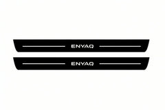 Catalogue illustration of two front black Matte PRO LED door sill plates with illuminated Enyaq lettering for Škoda Enyaq; dimensions are selected during manufacture.