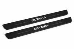 Shared catalogue demonstration of two black Matte PRO front plates with OCTAVIA lettering and straight lines for the Octavia Combi NX5 design; dark edges unlit. FRONT+REAR adds two rear plates not pictured; final dimensions selected during manufacture.