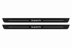 Catalogue demonstration of two black Matte PRO front door sill plates with mixed-case SuperB lettering and straight decorative side lines for Škoda Superb Combi 3T5; dark side edges unlit. FRONT+REAR adds two rear plates not pictured; dimensions selected during manufacture.