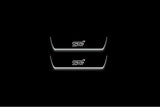 Two short door sill plates with STI lettering and edges illuminated in white, straight-on view on a dark background.