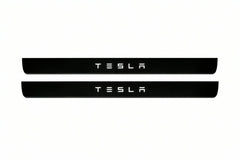 Catalogue illustration of two front black Matte PRO LED door sill plates with illuminated TESLA lettering for Tesla Model S; dimensions are selected during manufacture.