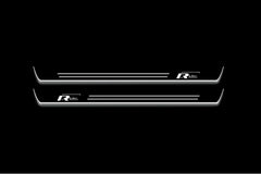 Two long door sill plates with R-Line with offset lettering lettering and edges illuminated in white, straight-on view on a dark background.