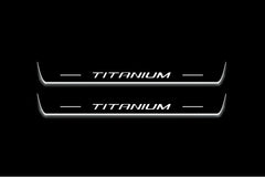 Two long door sill plates with Titanium lettering and edges illuminated in white, straight-on view on a dark background.