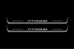 Two long door sill plates with Titanium lettering and edges illuminated in white, straight-on view on a dark background.
