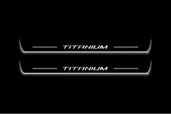 Two long door sill plates with Titanium lettering and edges illuminated in white, straight-on view on a dark background.