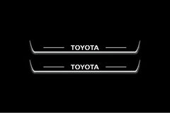 Two long door sill plates with Toyota lettering and edges illuminated in white, straight-on view on a dark background.