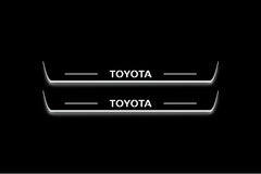 Two long door sill plates with Toyota lettering and edges illuminated in white, straight-on view on a dark background.