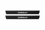 Catalogue illustration of two black Matte PRO front door sill plates with illuminated stylized COROLLA lettering on the top surface. Decorative lines and edges are unlit; rear plates for FRONT+REAR are not pictured. Final dimensions are selected for the Toyota Corolla E210 during manufacture.