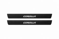 Catalogue illustration of two black Matte PRO front door sill plates with illuminated stylized COROLLA lettering on the top surface. Decorative lines and edges are unlit; rear plates for FRONT+REAR are not pictured. Final dimensions are selected for the Toyota Corolla E210 during manufacture.