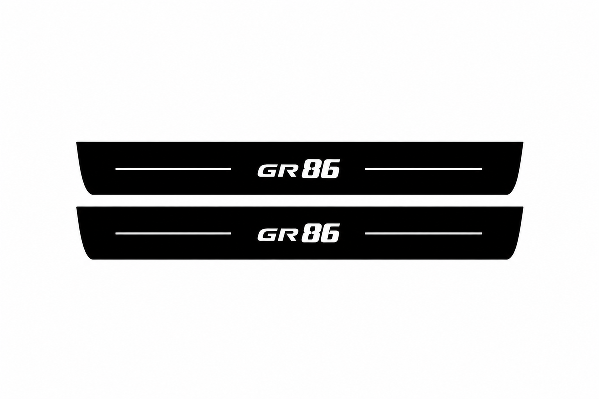 Catalogue illustration of two black Matte PRO front door sill plates with white GR86 lettering and thin horizontal lines on the top surface. Rear plates for FRONT+REAR are not pictured; final dimensions are selected for the vehicle during manufacture.