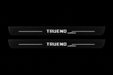 Catalogue illustration of two black Matte PRO front door sill plates with white TRUENO and lowercase italic edition lettering and thin lines illuminated only on the top surface. Rear plates for FRONT+REAR are not pictured; final dimensions are selected for the vehicle during manufacture.
