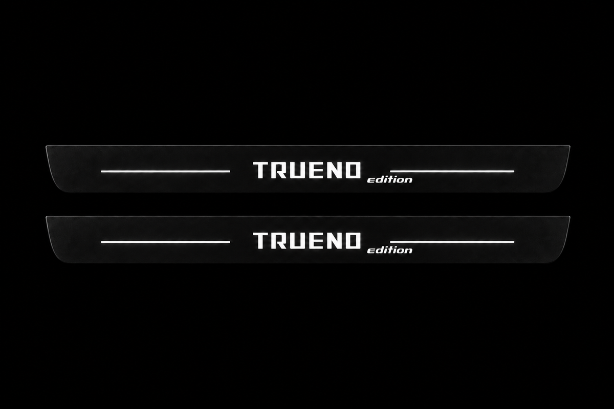 Catalogue illustration of two black Matte PRO front door sill plates with white TRUENO and lowercase italic edition lettering and thin lines illuminated only on the top surface. Rear plates for FRONT+REAR are not pictured; final dimensions are selected for the vehicle during manufacture.
