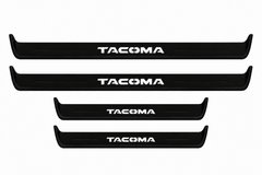 Catalogue illustration of two long black Matte PRO front sill plates and two shorter rear plates with TACOMA lettering illuminated on top. Side edges unlit; vehicle-specific dimensions are not depicted. FRONT option includes front plates only.