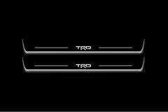 Two long door sill plates with TRD lettering and edges illuminated in white, straight-on view on a dark background.