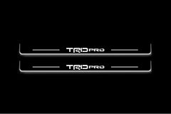 Two long door sill plates with TRD Pro lettering and edges illuminated in white, straight-on view on a dark background.