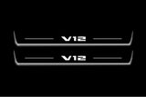 Two long door sill plates with V12 lettering and edges illuminated in white, straight-on view on a dark background.