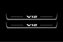 Two long door sill plates with V12 lettering and edges illuminated in white, straight-on view on a dark background.
