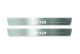Two long silver-finished door sill plates with V12 lettering on a light background, straight-on view.