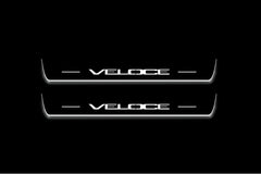 Two long door sill plates with Veloce lettering and edges illuminated in white, straight-on view on a dark background.