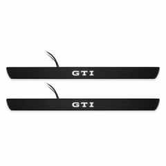 Catalogue illustration of two black Matte PRO front door sill plates with white GTI lettering illuminated only on top. Edges are unlit; rear plates for FRONT+REAR are not pictured. Final dimensions are selected for Golf Mk8 GTI during manufacture.