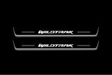 Two long door sill plates with Wildtrak lettering and edges illuminated in white, straight-on view on a dark background.