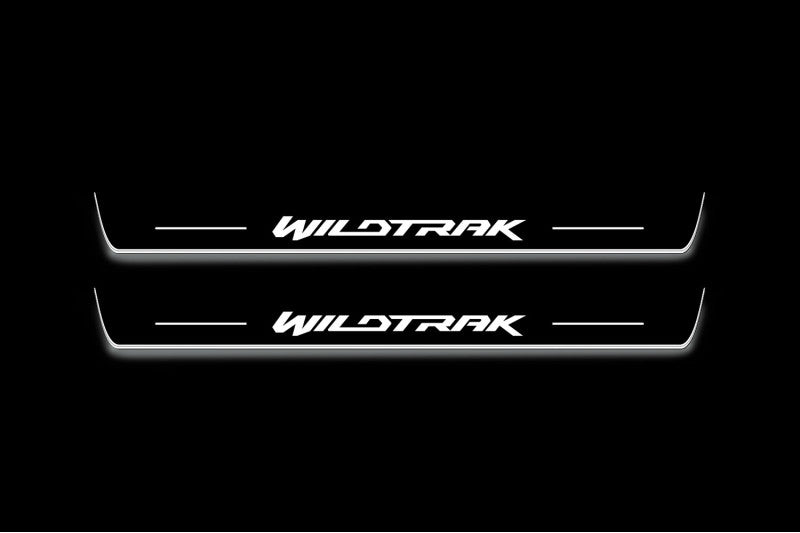 Two long door sill plates with Wildtrak lettering and edges illuminated in white, straight-on view on a dark background.