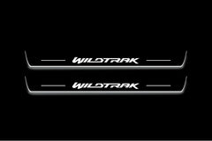 Two long door sill plates with Wildtrak lettering and edges illuminated in white, straight-on view on a dark background.