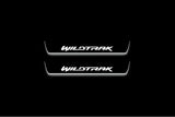 Two short door sill plates with Wildtrak lettering and edges illuminated in white, straight-on view on a dark background.