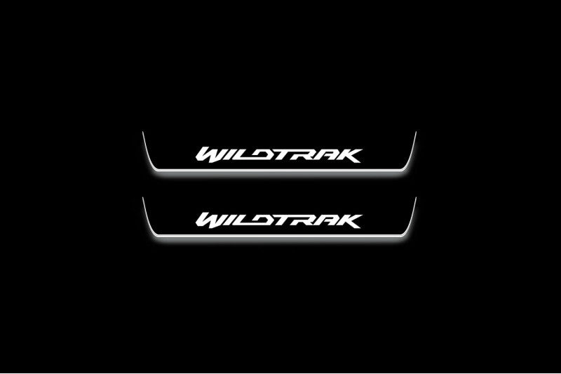 Two short door sill plates with Wildtrak lettering and edges illuminated in white, straight-on view on a dark background.