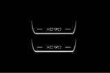 Two short door sill plates with XC90 lettering and edges illuminated in white, straight-on view on a dark background.