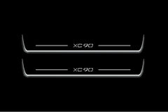 Two long door sill plates with XC90 lettering and edges illuminated in white, straight-on view on a dark background.