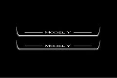 Two long door sill plates with Model Y lettering and edges illuminated in white, straight-on view on a dark background.