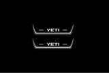 Two short door sill plates with Yeti lettering and edges illuminated in white, straight-on view on a dark background.