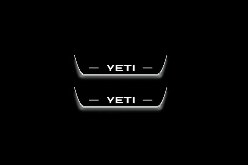 Two short door sill plates with Yeti lettering and edges illuminated in white, straight-on view on a dark background.